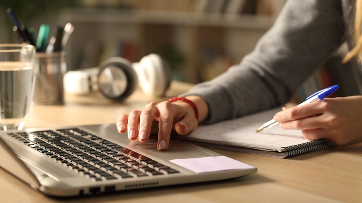 Person using a laptop and writing in a notepad